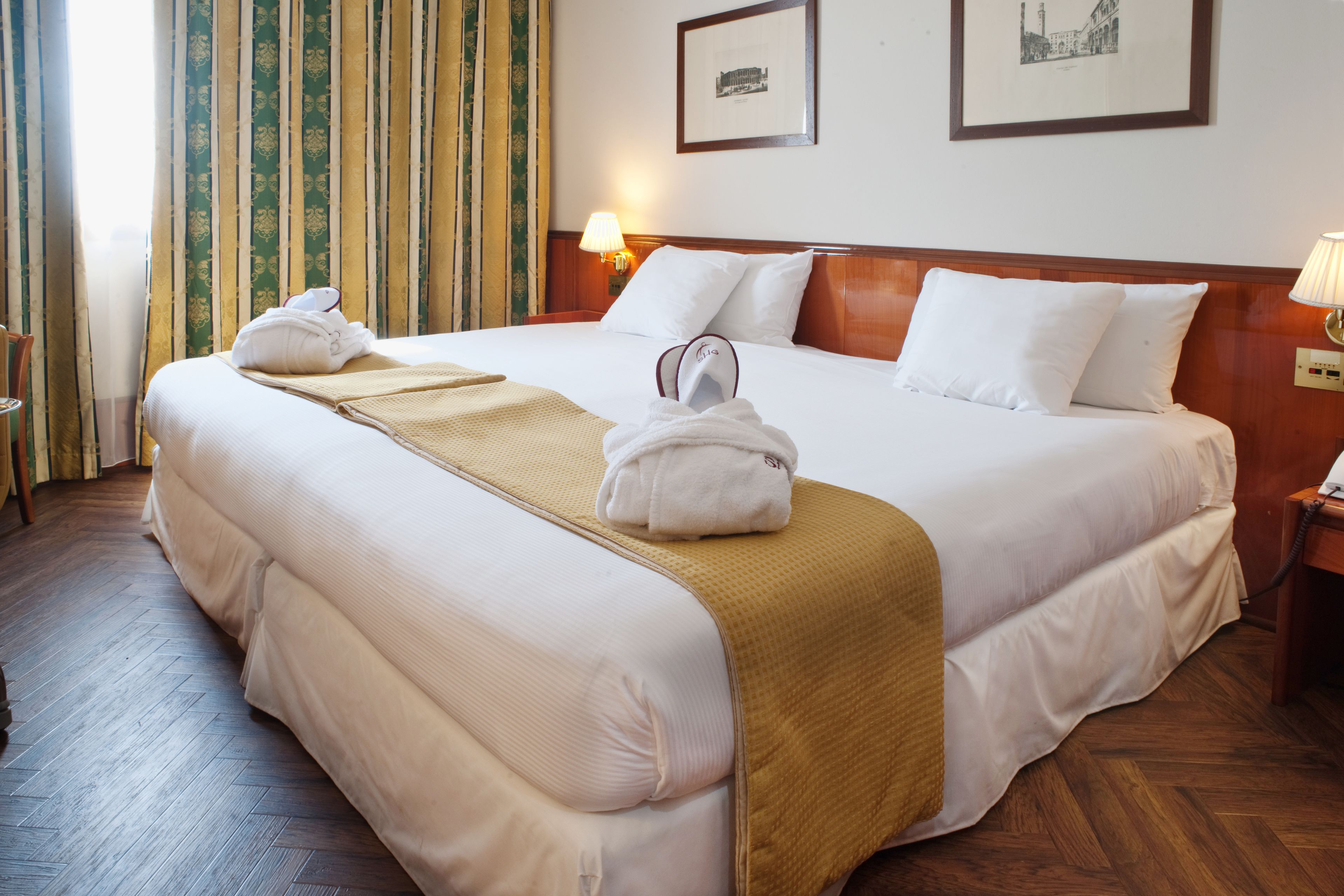 Ein Hotelzimmer mit einem großen Bett, einem hölzernen Kopfteil, zwei Nachttischlampen, einem gerahmten Bild an der Wand und einem Holzboden.