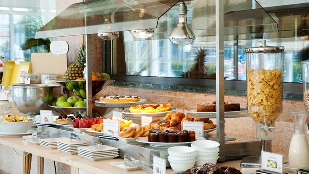 A buffet with various food items and a glass container of cereal.