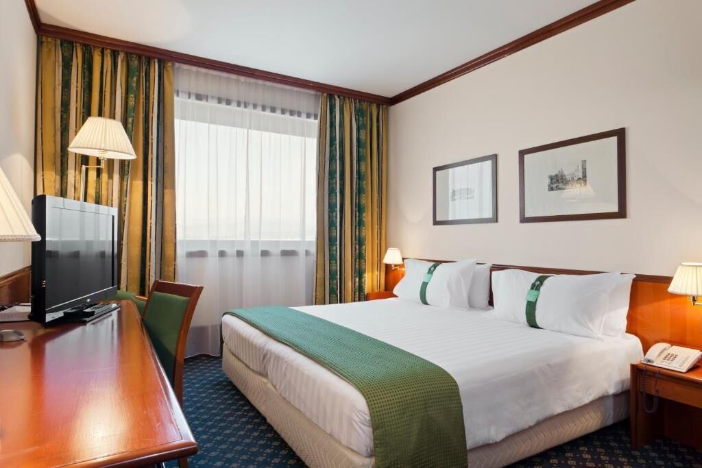 A hotel room with a bed, a desk with a television, a chair, a lamp, and a telephone.