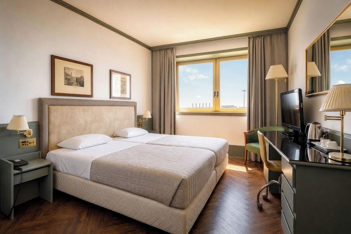 Habitación de hotel con cama doble, escritorio con computadora, televisión y ventana con cortinas.