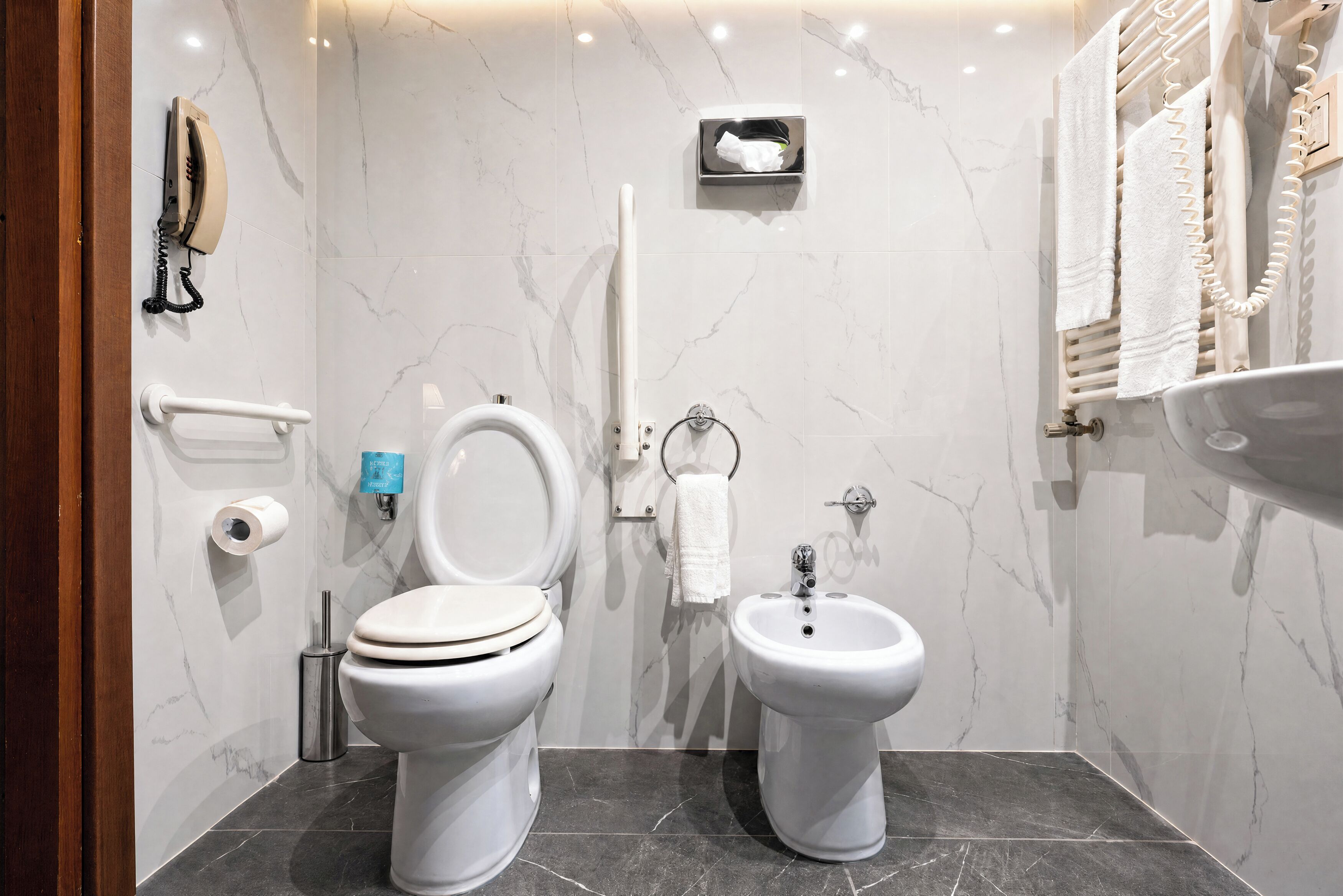 A modern bathroom with a toilet, bidet, towel rack, and a hand dryer.