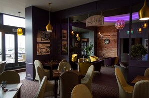 L’intérieur d’un restaurant, avec des chaises et des tables en osier, ainsi que des lampes suspendues.