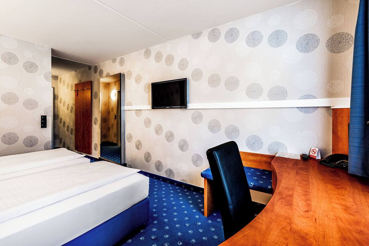Une chambre d’hôtel équipée d’un lit, d’un bureau, d’une chaise, d’une télévision et d’une porte donnant sur une autre pièce.