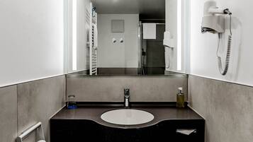 A modern bathroom with a large mirror, a sink, and a hairdryer mounted on the wall.