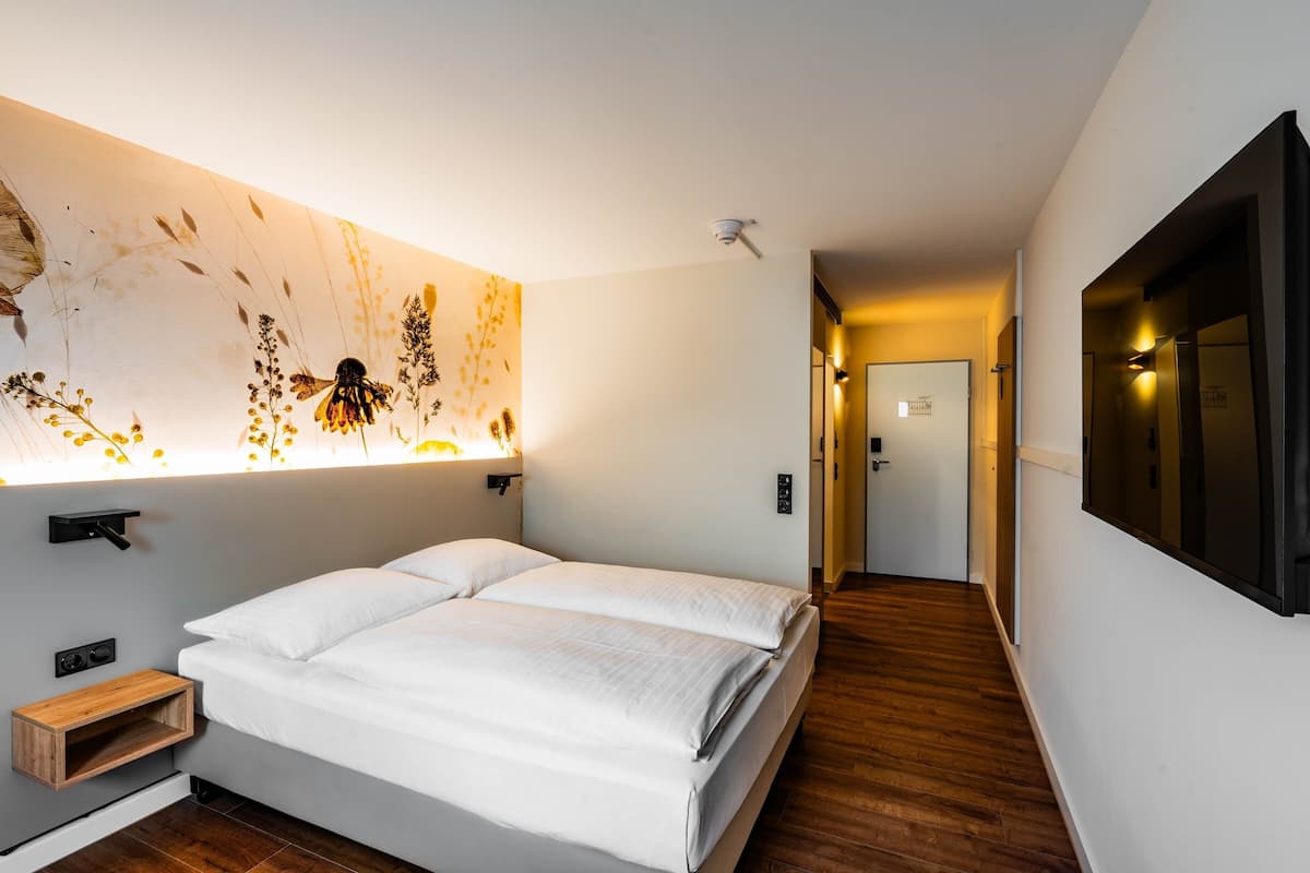 Une chambre d’hôtel moderne avec un grand lit, un luminaire mural décoratif et un plancher en bois.