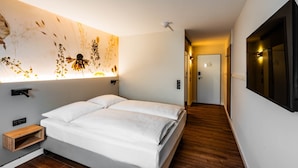 Ett modernt hotellrum med en stor säng, en väggmonterad lampa och ett trägolv.