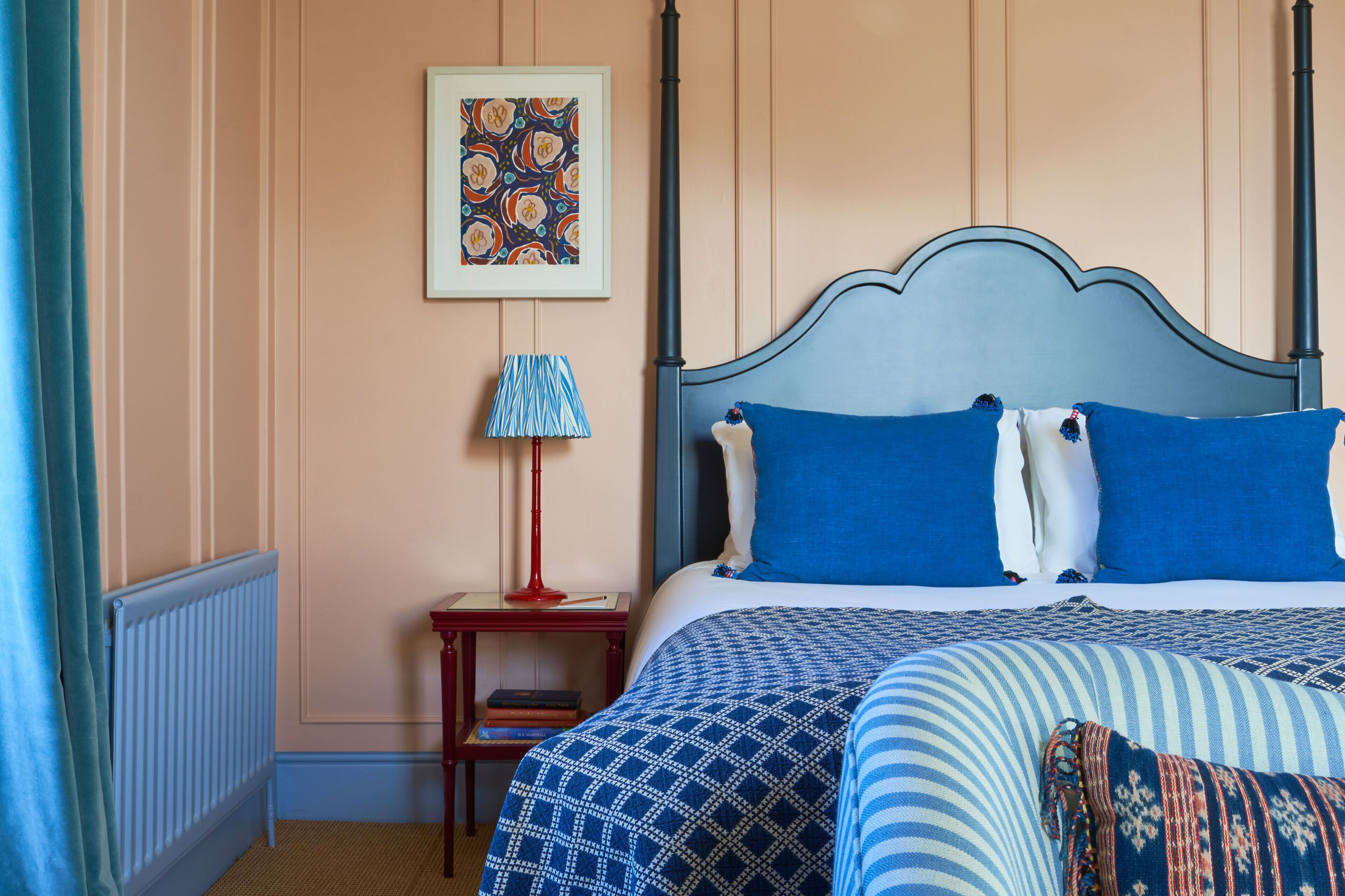 A bedroom with a four-poster bed, a red nightstand with a lamp, and a framed picture on the wall.