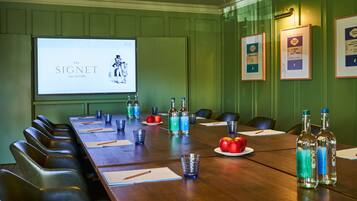 A conference room with a long table, chairs, a projector screen, and framed certificates on the wall.