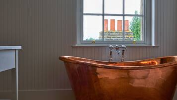 A bathroom with a copper bathtub, a window with a view of buildings, and wooden paneling on the walls.