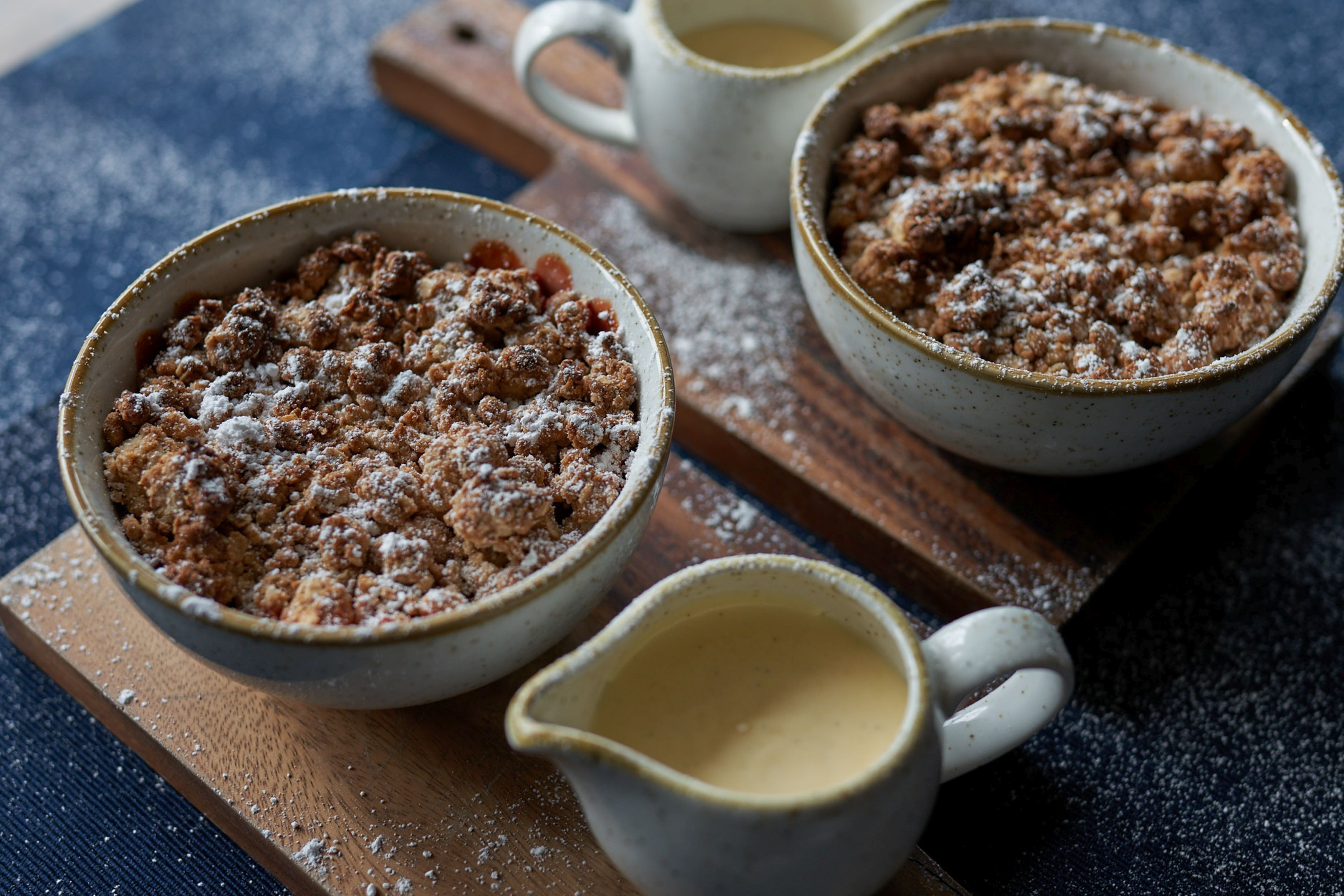 Twee dessertkommen op een houten plank, met een klein kannetje room.