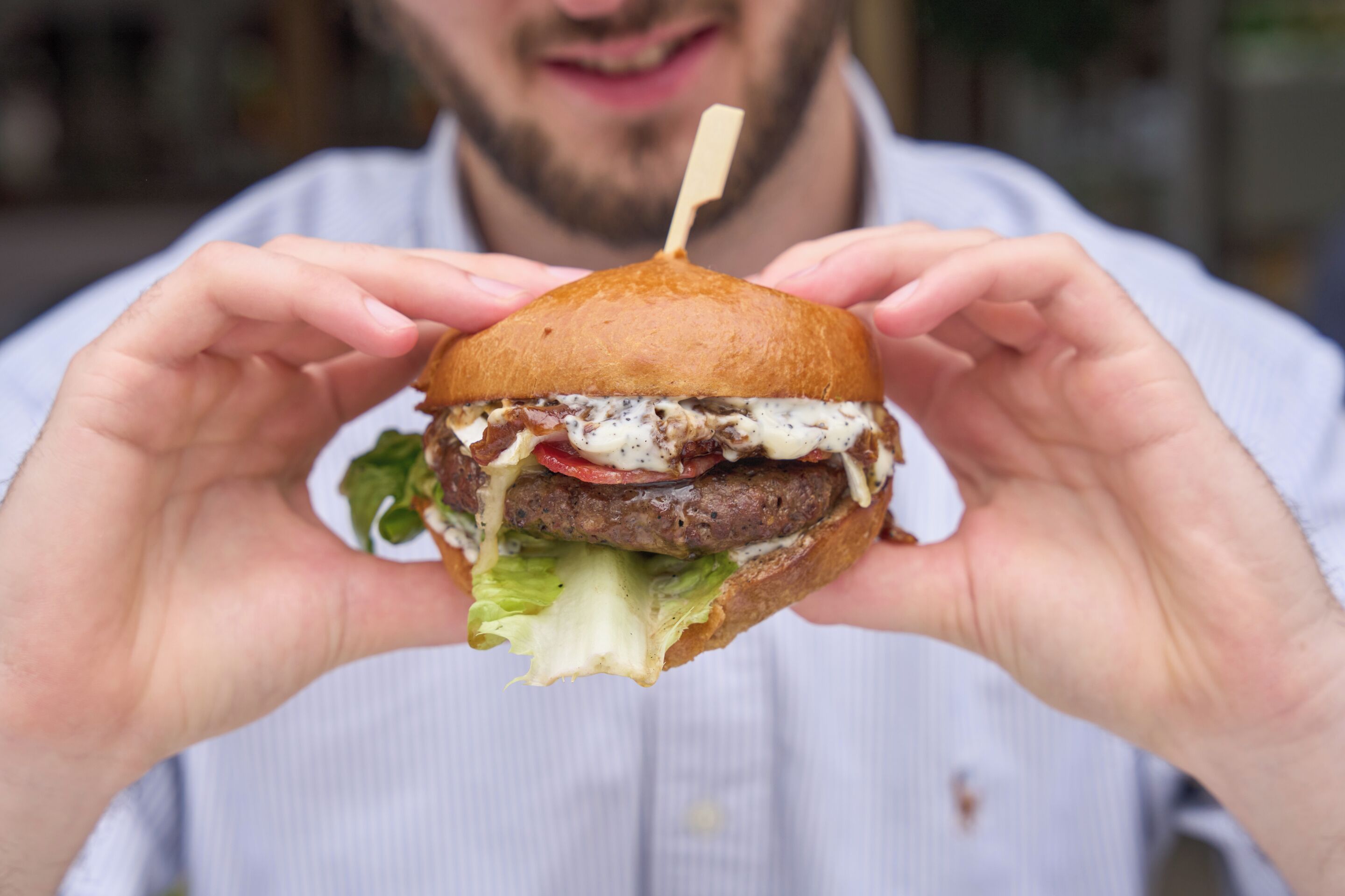 A person holding a burger with a toothpick in the center.