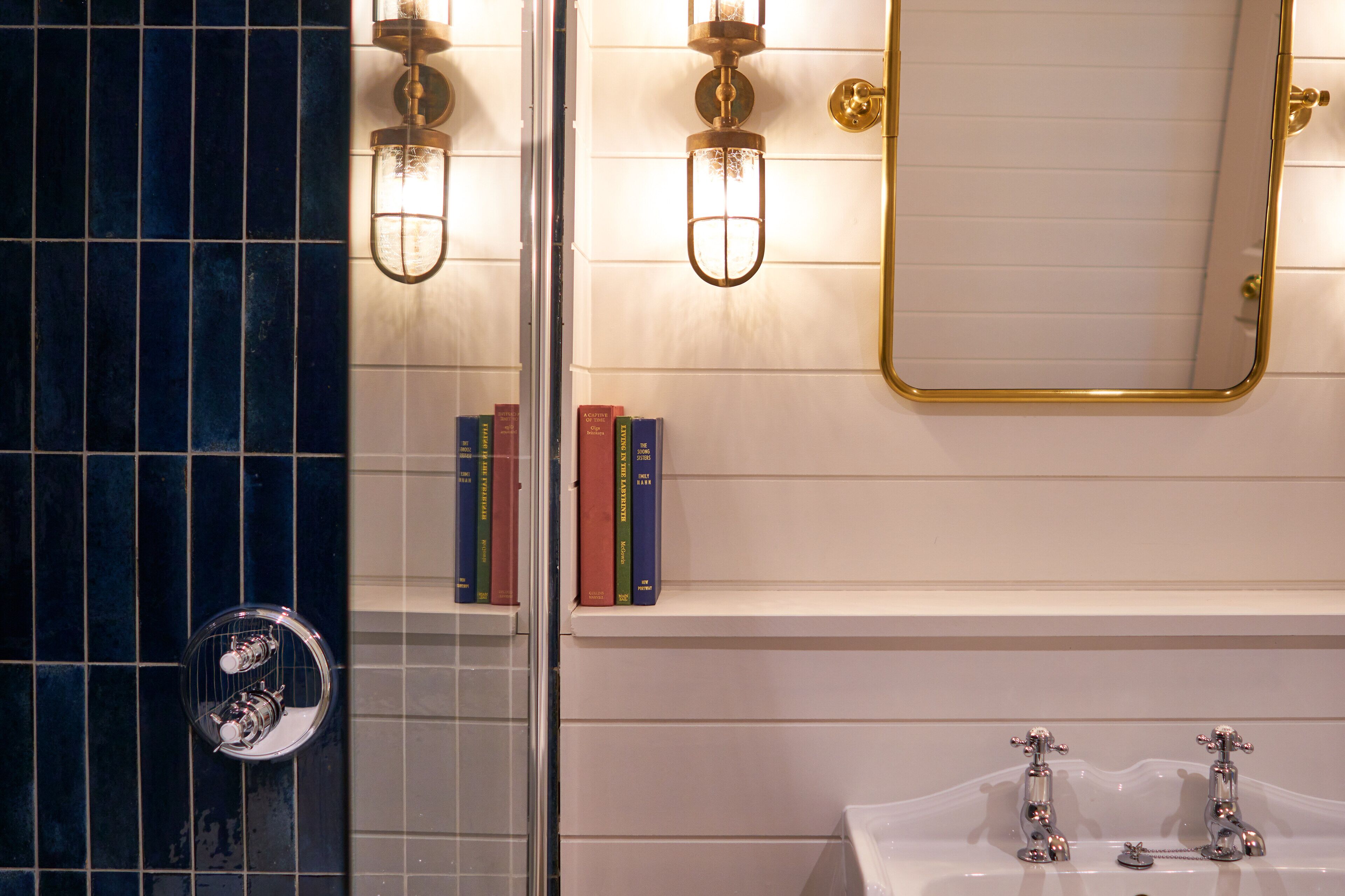 A bathroom with a white sink, two chrome faucets, a mirror with a gold frame, and two wall-mounted light fixtures.