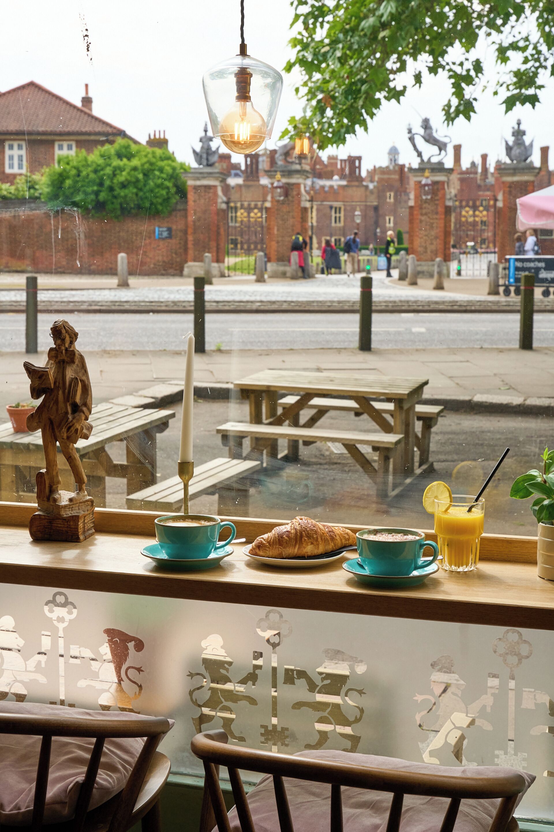 A café with a view of a historic building, outdoor seating, and a statue.