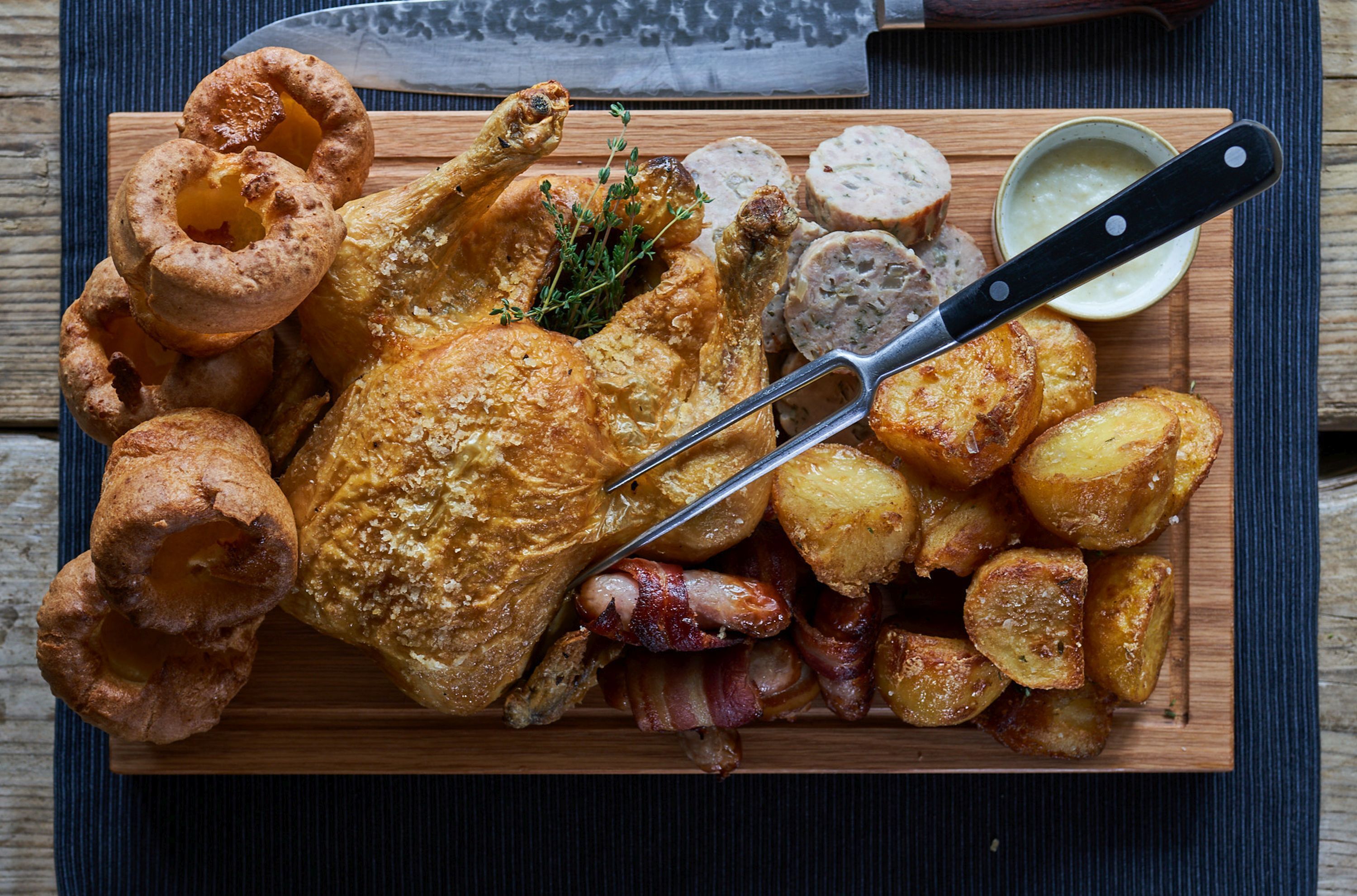 A roasted chicken with potatoes and Yorkshire puddings on a wooden board.