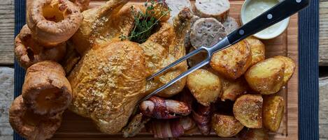 A roasted chicken with potatoes and Yorkshire puddings on a wooden board.