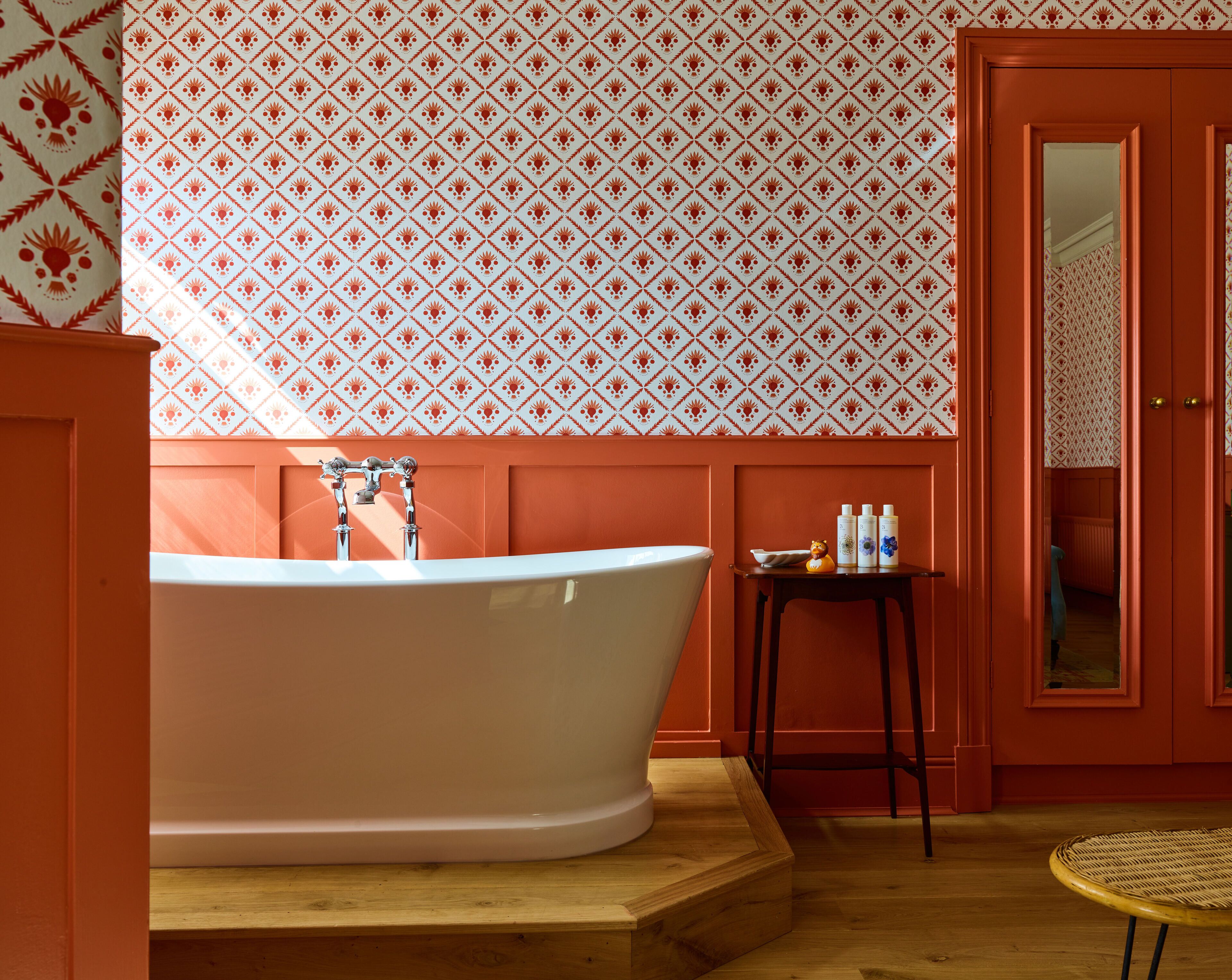 A bathroom with a freestanding bathtub, wooden flooring, and a patterned wallpaper.
