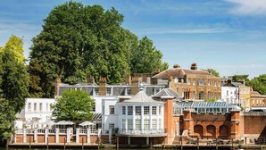 A riverside hotel with a white facade, brick buildings, and a large tree in the background. - The Mitre, Hampton Court (East Molesey)