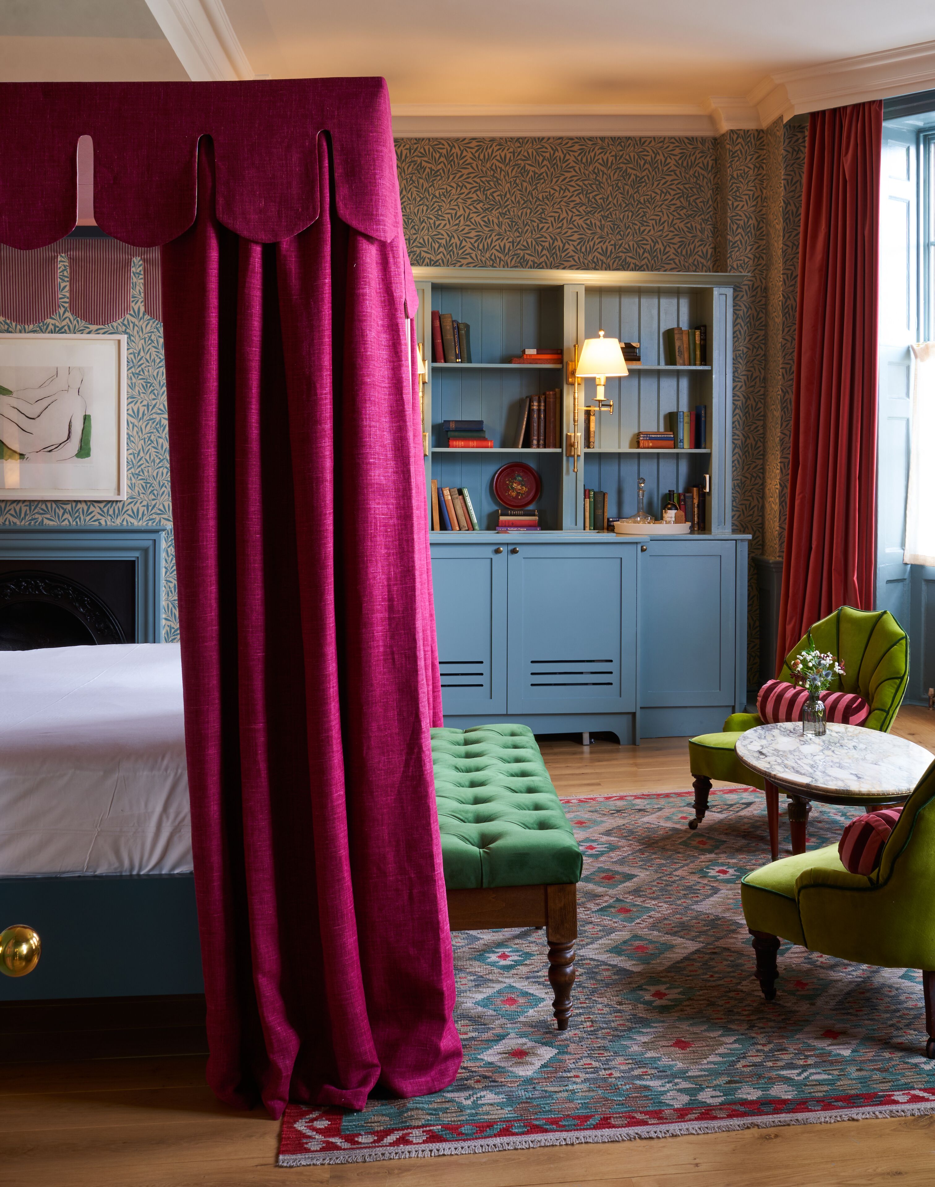 Camera da letto con un letto a baldacchino, una panca imbottita verde, un tavolino con un vaso e una libreria blu.