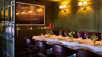 Un restaurant avec une longue table dressée pour le repas, un tableau accroché au mur et des lampes fixées au mur.