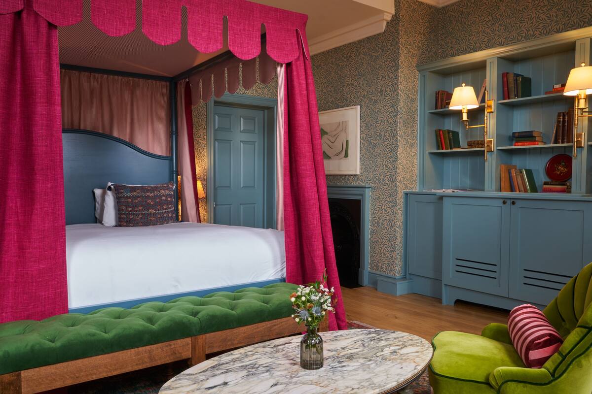 A bedroom with a four-poster bed, green upholstered bench, a marble table, and a green armchair.