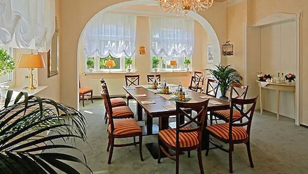 Uma sala de jantar com uma mesa comprida, cadeiras e um lustre.