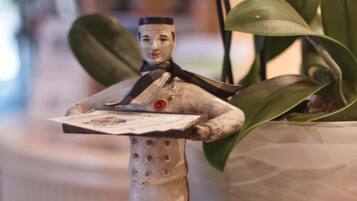 A small figurine of a person holding a shield, placed on a wooden surface with a potted plant in the background.