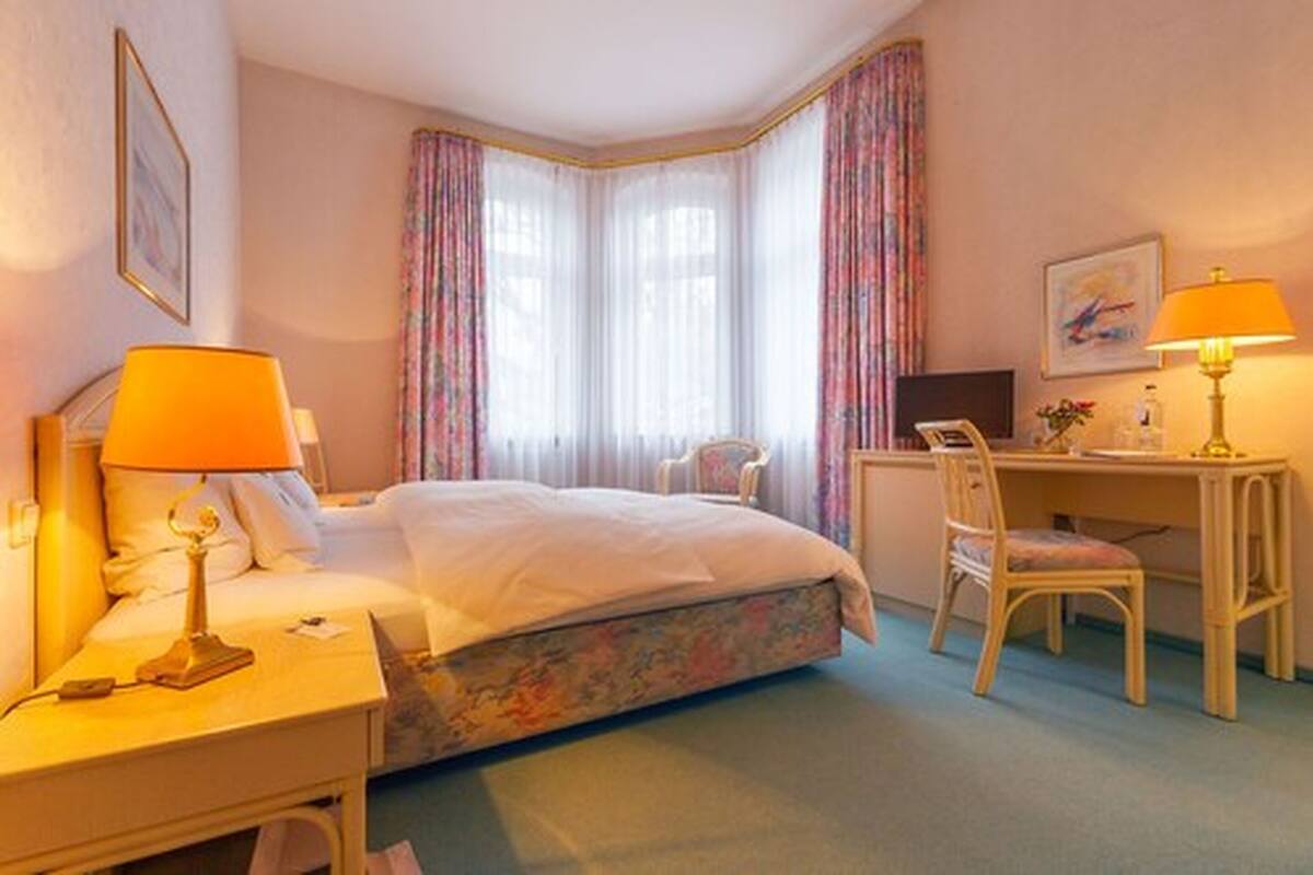 A hotel room with a bed, a desk, a chair, and a window with curtains.