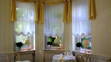 Un comedor con una mesa lista para cuatro personas, dos sillas y una ventana con cortinas.