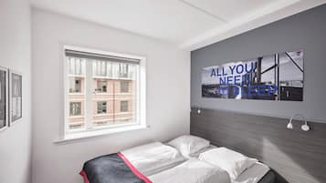 A modern hotel room with a large bed, a window with a view of a brick building, and a wall-mounted artwork with text.