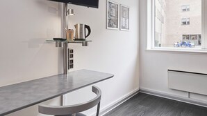 A modern room with a flat-screen TV mounted on the wall, a glass shelf with a kettle, a coffee machine, and framed pictures.
