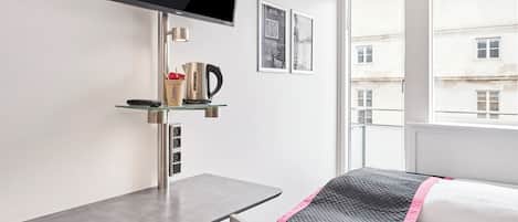 Habitación de hotel moderna con cama, escritorio con silla, televisión de pantalla plana y ventana con vistas a edificios.