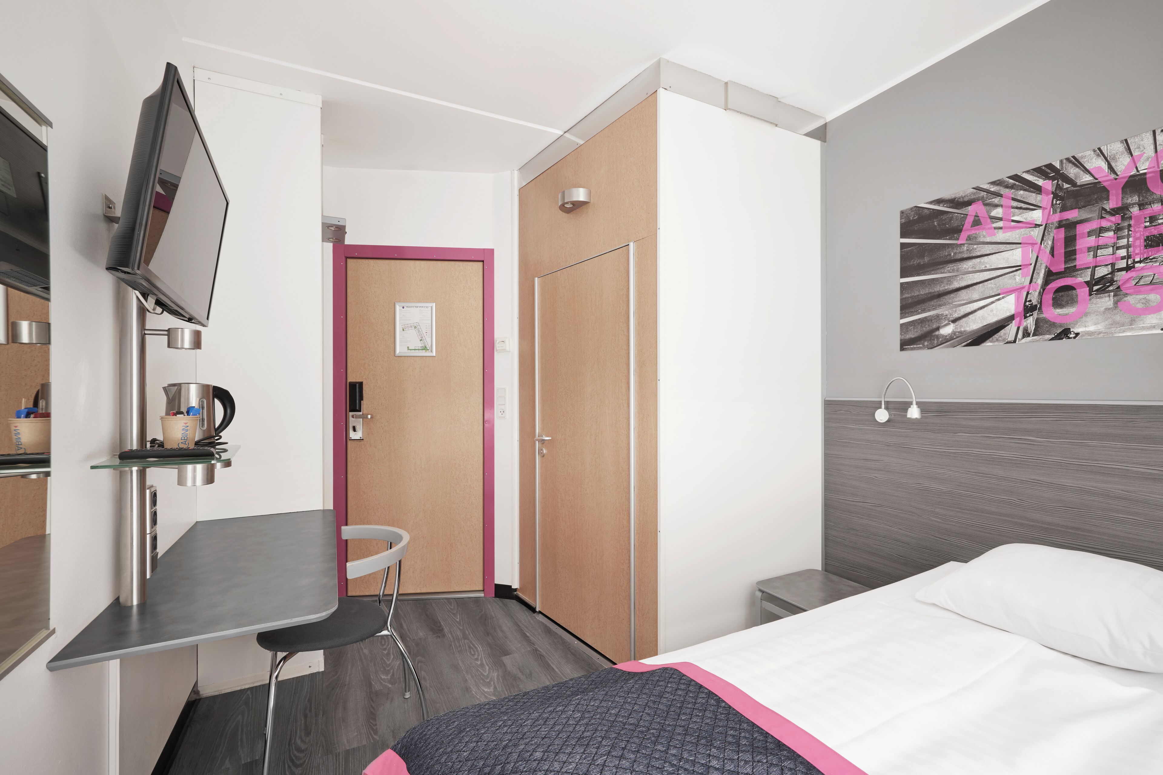 Une chambre d’hôtel moderne équipée d’un lit, d’un bureau, d’une chaise, d’une télévision et d’une porte donnant sur une autre pièce.