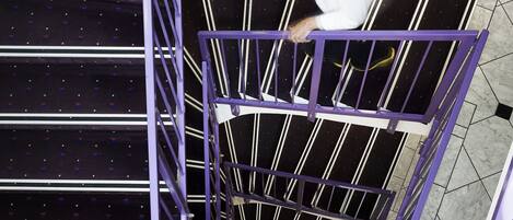Un escalier en colimaçon avec des rampes violettes, et une personne qui monte.
