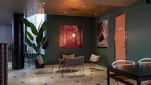 A modern lounge area with a large potted plant, a table with chairs, and a wall with a 'SAME LOVE RATHER ROUND' sign.