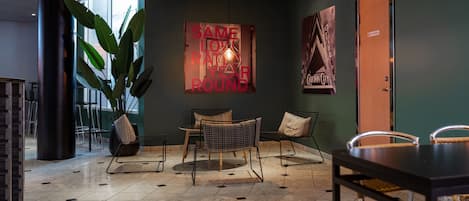 A modern lounge area with a large potted plant, a table with chairs, and a wall with a 'SAME LOVE RATHER ROUND' sign.