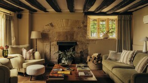 Una sala de estar acogedora con chimenea de piedra, un sofá, una mesita con libros y una ventana con cortinas.