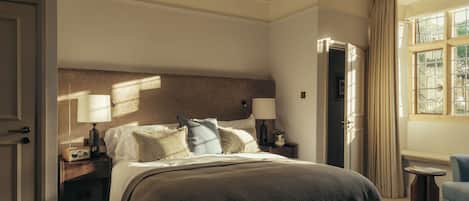 Un dormitorio con una cama grande, lámparas de noche, una mesita de noche, una silla y una ventana con cortinas.