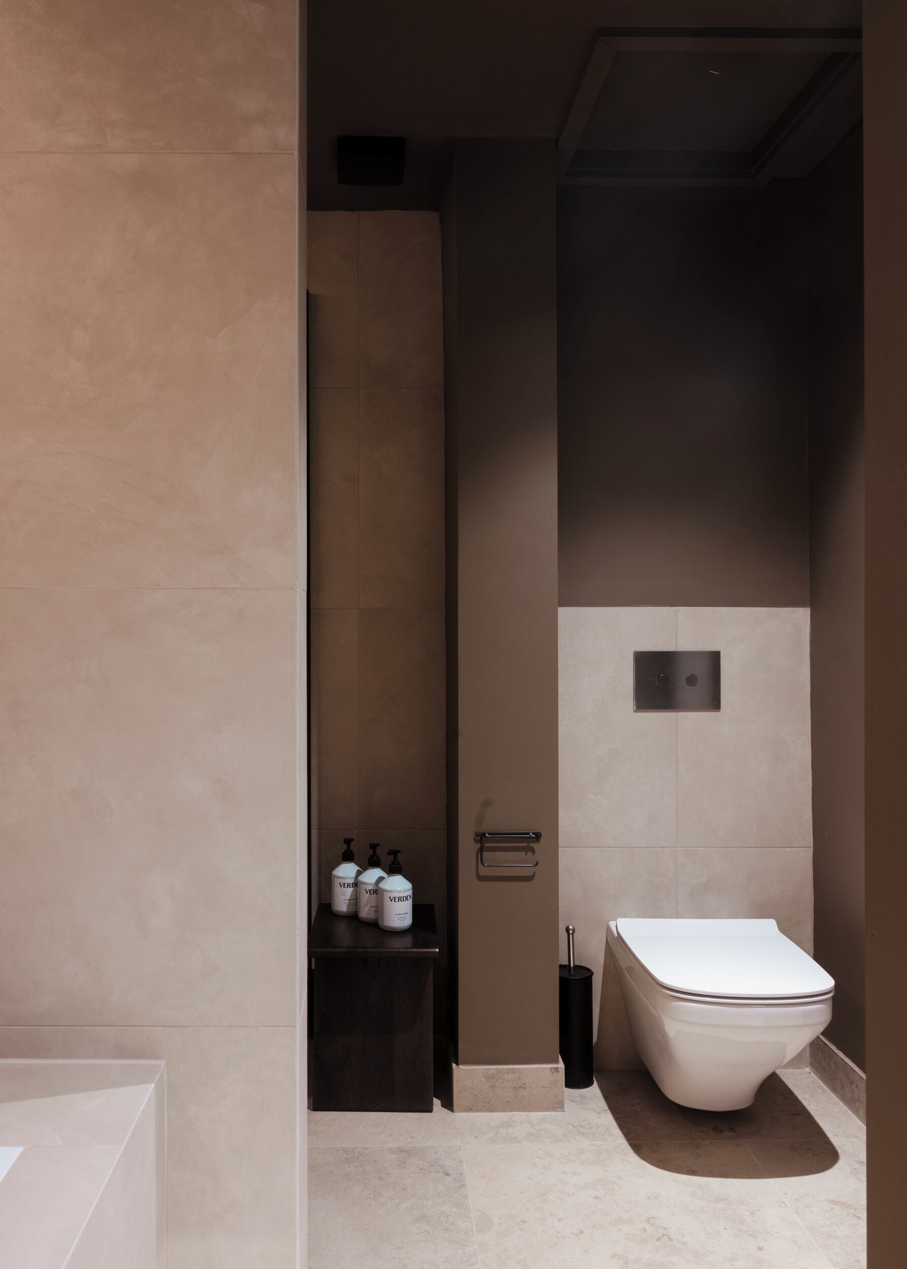 Un baño moderno con inodoro blanco, estante con artículos de aseo y un cubo de basura negro.