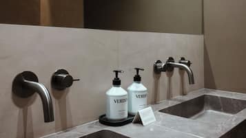 Een moderne badkamer met twee wastafels, elk met een kraan en een zeepdispenser.