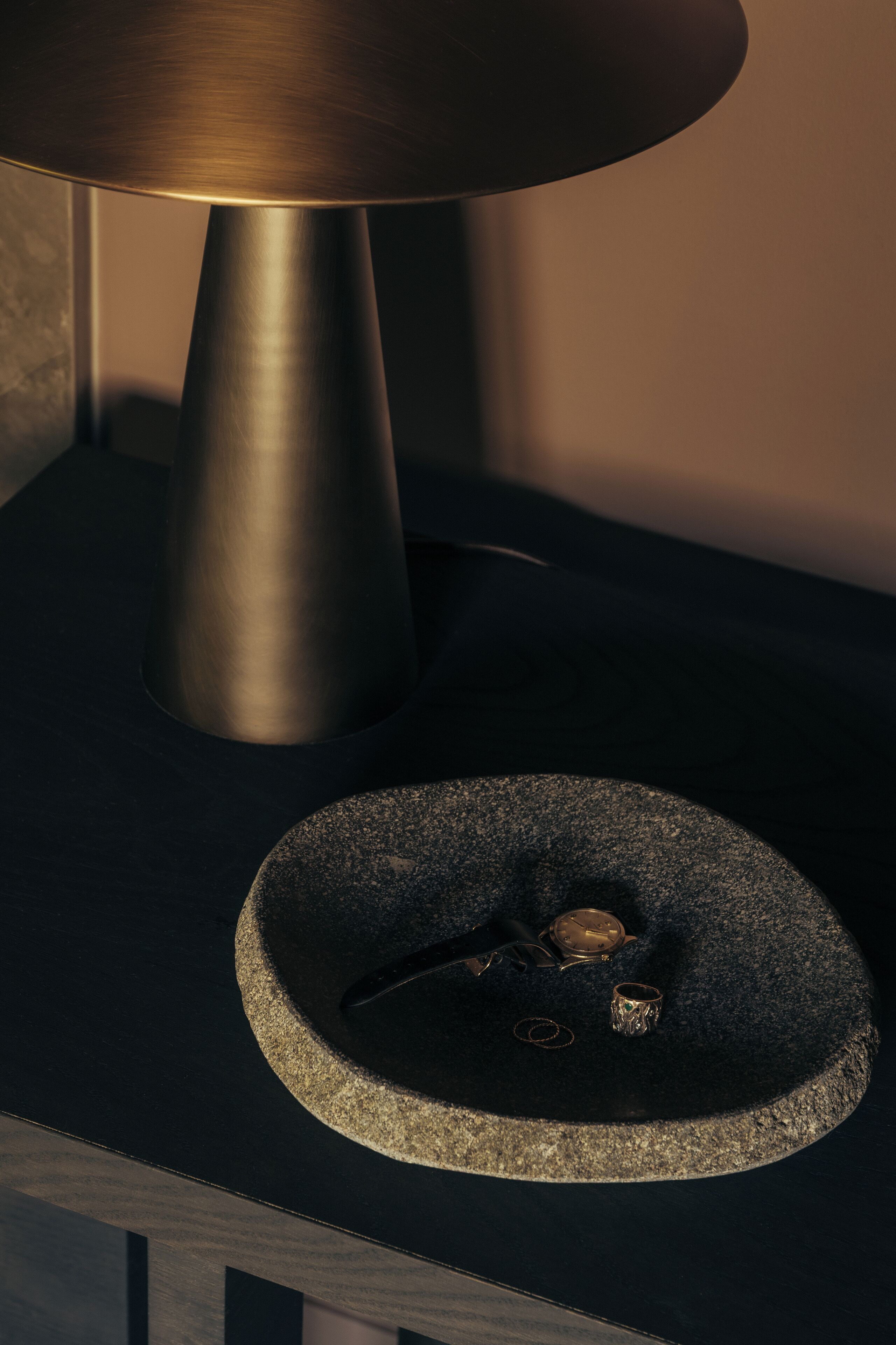A modern lamp with a metallic shade and a stone base on a dark surface.