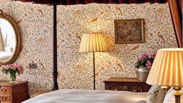 Un dormitorio con cama, mesita de noche, lámpara, cómoda, espejo y papel tapiz con motivos florales.