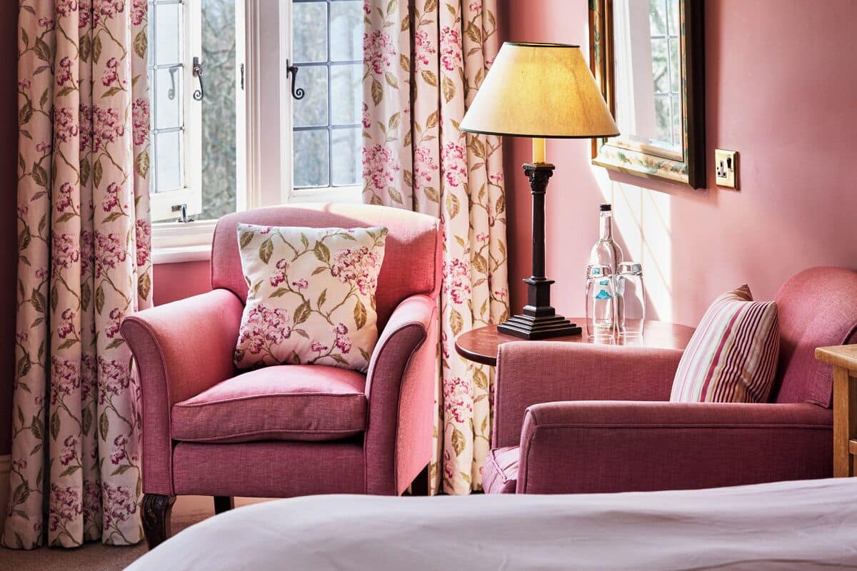 A pink-themed room with floral curtains, a lamp, and a bed.