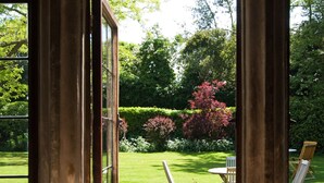 A view through a window with a metal grill, a garden with a lawn, and a chair.