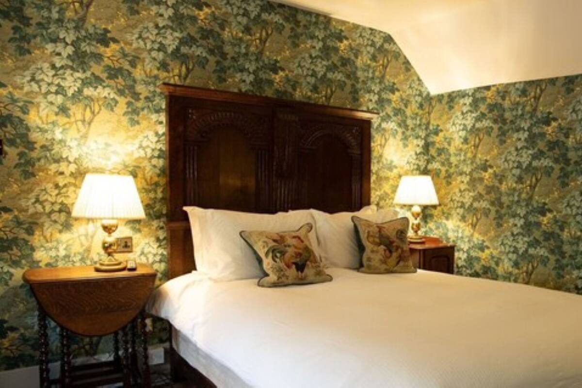 A bedroom with a large bed, floral wallpaper, two bedside lamps, and decorative pillows.