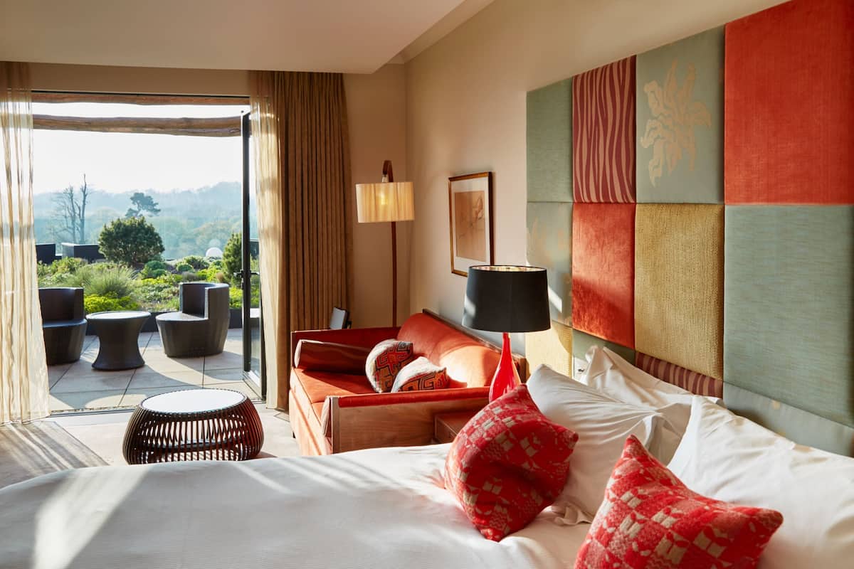 A hotel room with a bed, a sofa, a lamp, and a view of the outdoors.