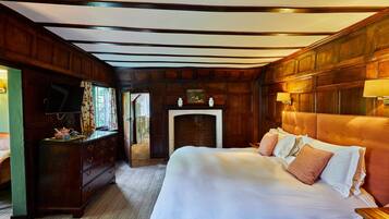 A room with a large bed, wooden paneling, a fireplace, and a television on a dresser.