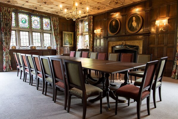 A formal dining room with a long table and chairs, large windows with stained glass, and a fireplace with portraits. - Ockenden Manor Hotel & Spa (Haywards Heath)
