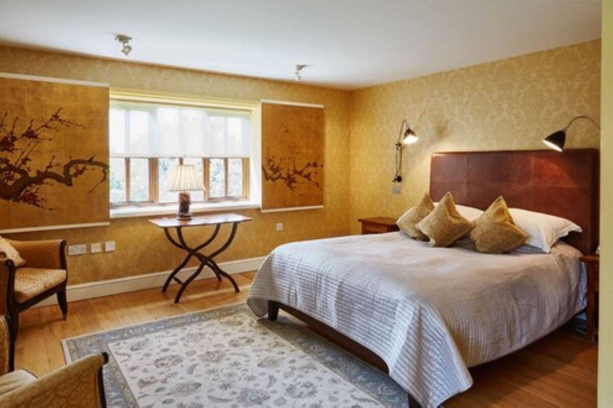 Une chambre avec un grand lit, une petite table, une chaise et une fenêtre avec des stores.