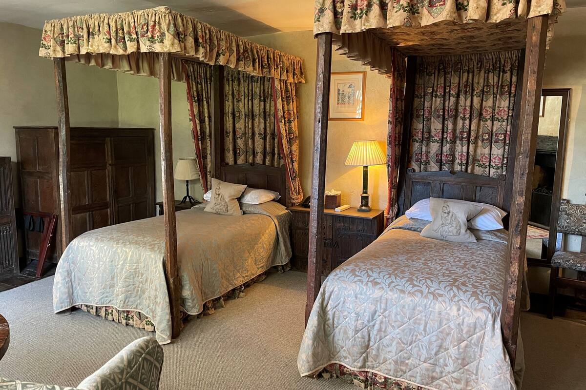Un lit traditionnel à baldaquin, agrémenté de rideaux à motifs floraux, d’une lampe de chevet et d’un tableau encadré au mur.