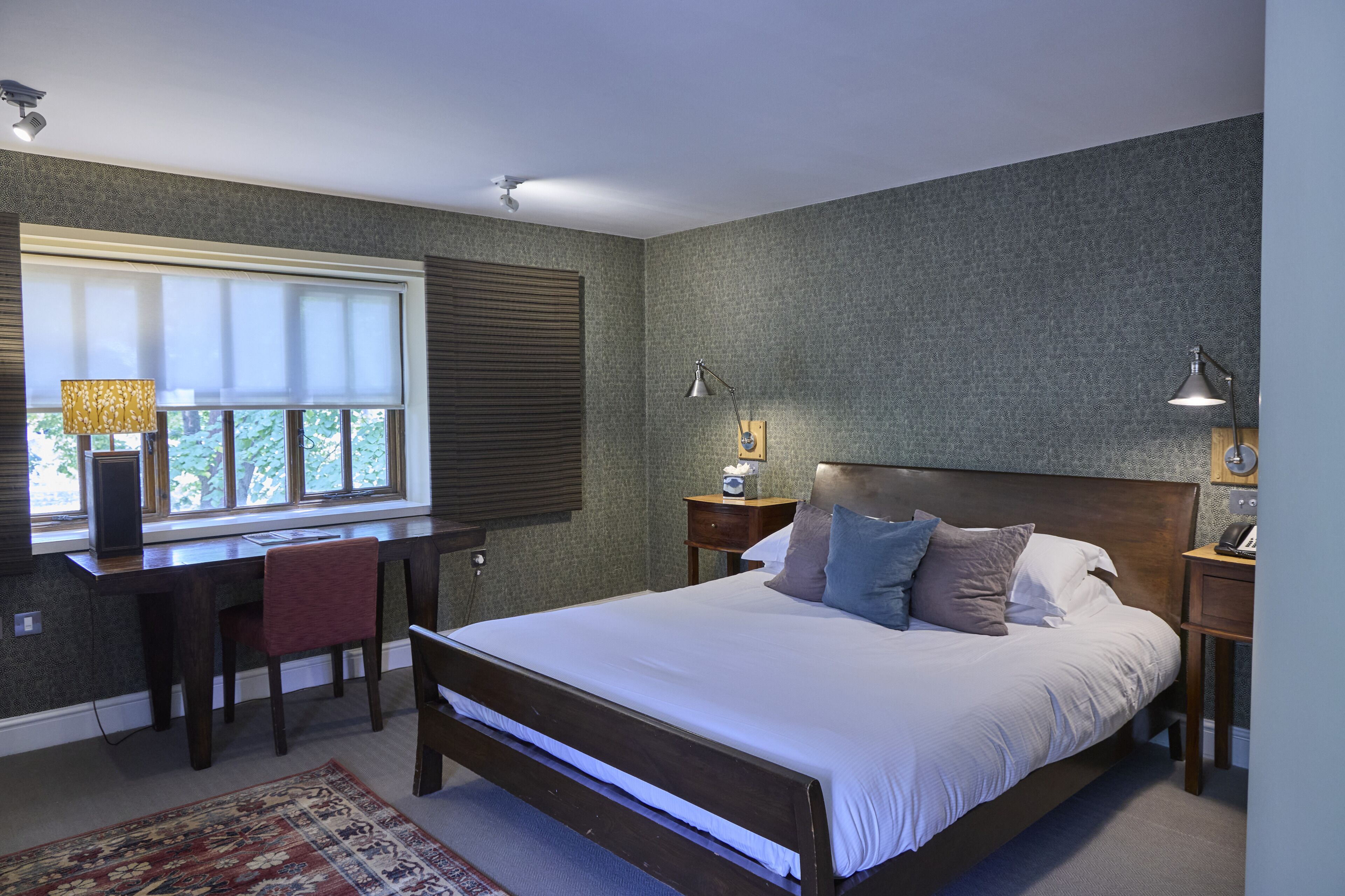 A bedroom with a large bed, a desk, and two bedside lamps.